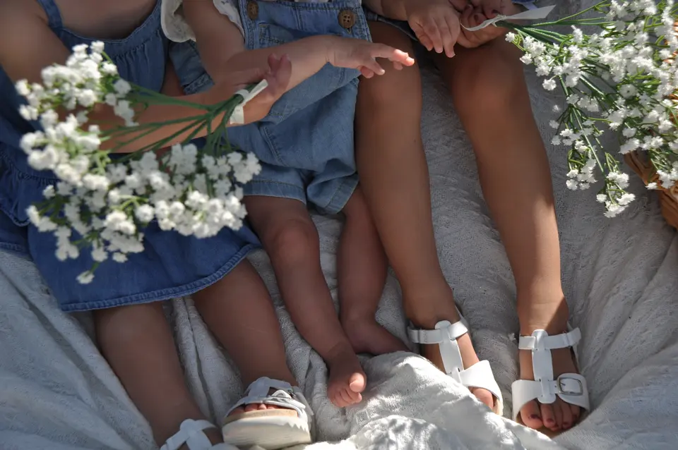 Children and a baby sitting together on a picnic blanket with white flowers