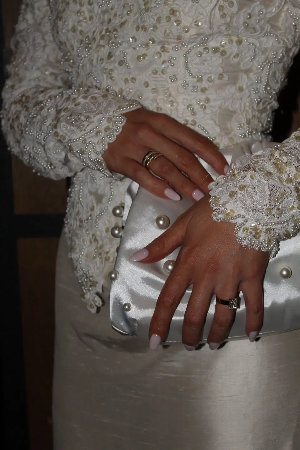 Close-up of a bride's rings, beaded lace sleeves and pearl-trimmed clutch