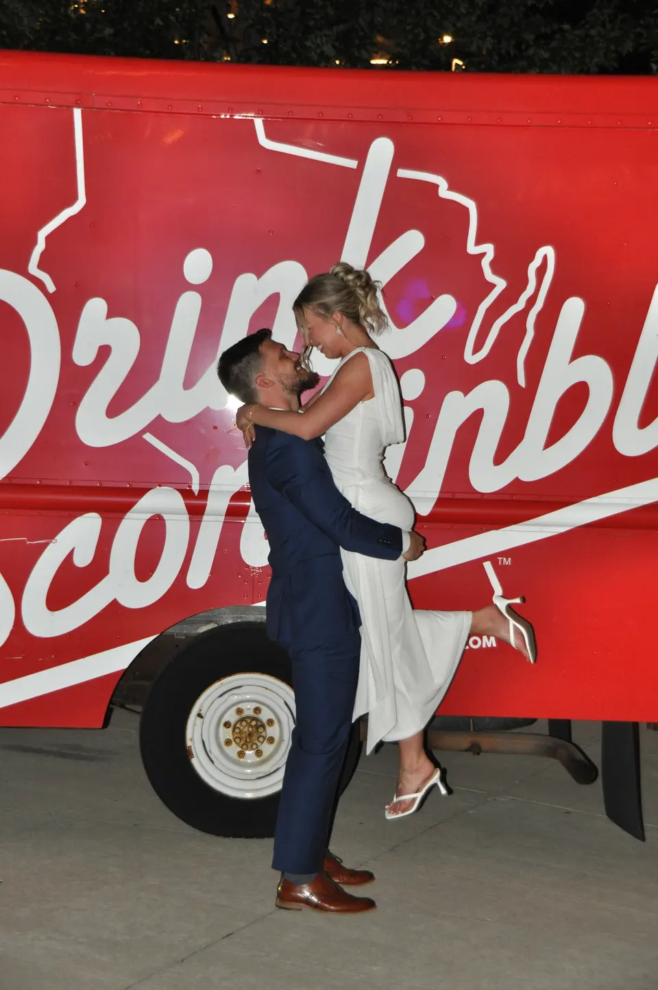 Newlyweds embracing in front of a red Drink Wisconsinbly trailer