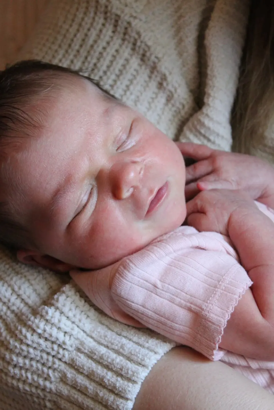 A sleeping newborn resting in a parent's hands